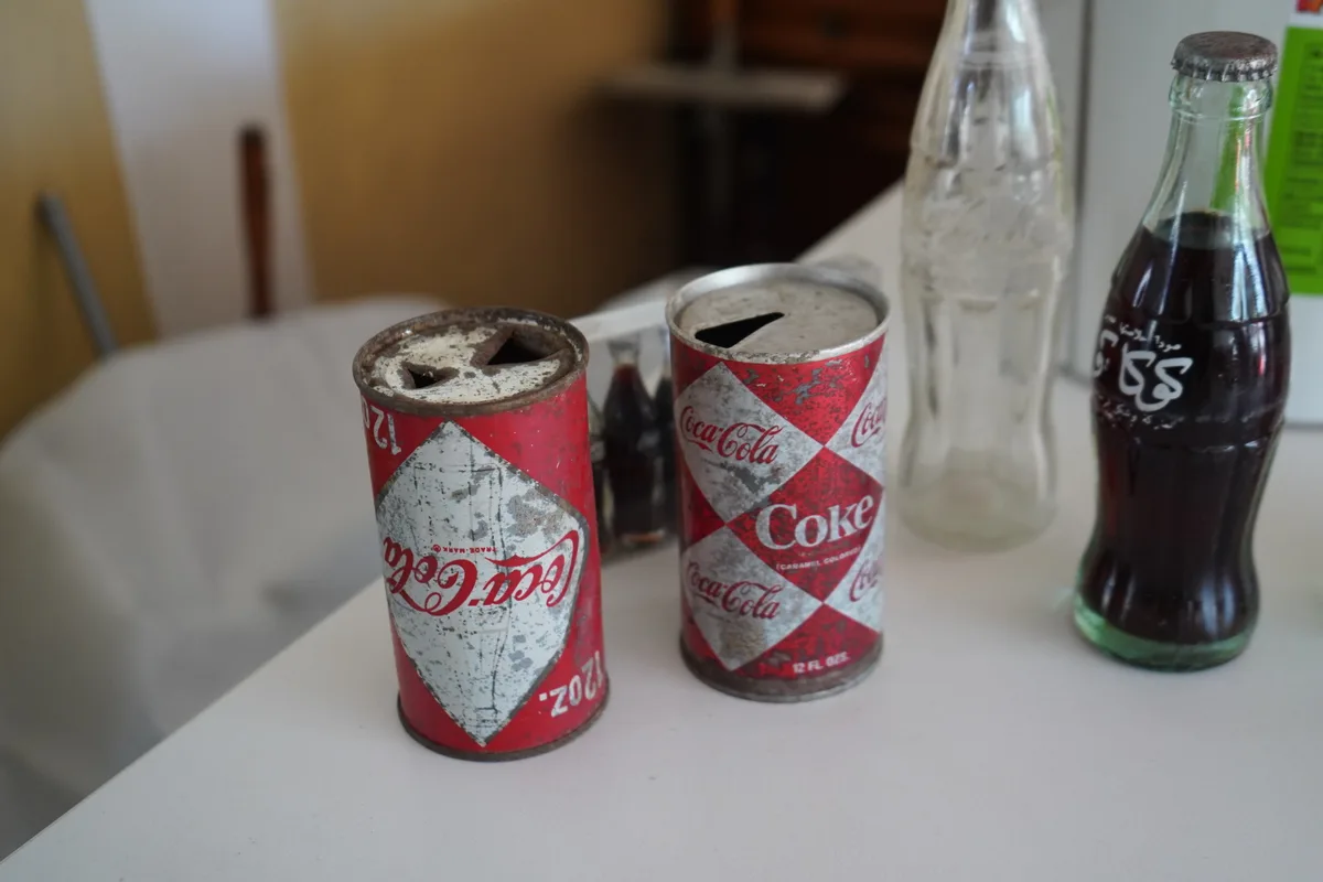 Man sieht zwei uralte, rostige Cola-Dosen.